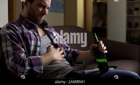 Alkoholabhängige leiden unter Magenschmerzen, halten Flasche in der Hand, ungesundes Leben Stockfoto