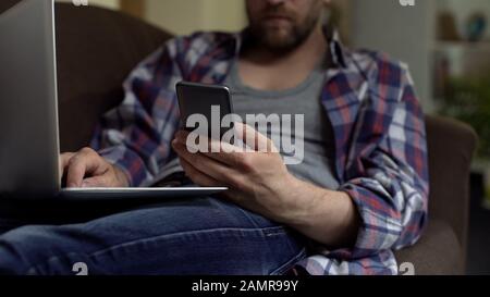 Mann mit Telefonanwendung und Arbeit auf Laptop, Online-Zahlungsbestätigung Stockfoto