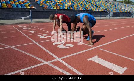 Zwei multirassische Athleten in der Startposition, bereit, nach dem Befehl zu laufen Stockfoto