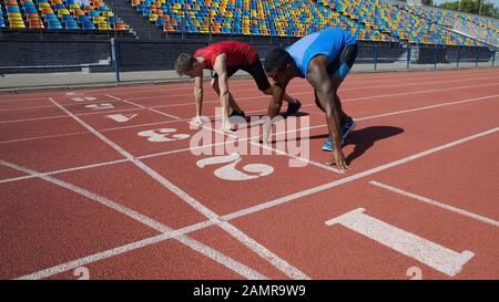 Multirassische Athleten in der Startposition, bereit für den Lauf nach dem Befehl, Marathon Stockfoto