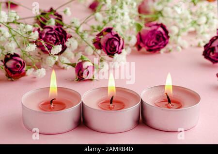 Aromatherapie-Konzept. Drei brennende Kerzen und trockene Rosen auf rosa Hintergrund. Stockfoto