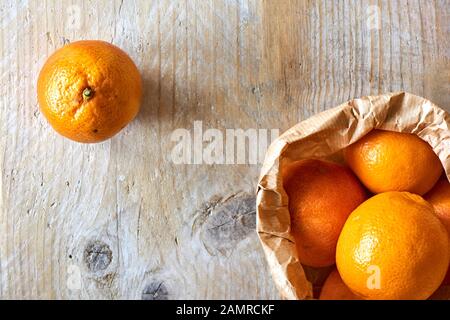 Orange Bio-Blutorangen in brauner Papiertüte auf verwittertem Holztisch mit Kopierraum. Flaches Lay. Stockfoto