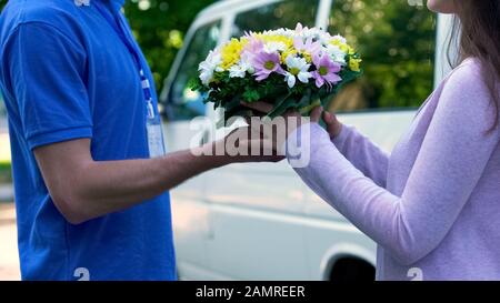 Überraschte Frau, die Blumenstrauß von den Kurierhänden, Blumenstrauß nahm Stockfoto