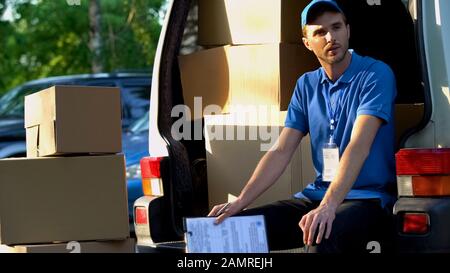Junger Mann aus dem Lieferdienst, im Lieferwagen sitzend, Paketverladung Stockfoto