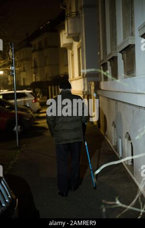 Perspektivische Straßenszene mit Silhouette eines älteren Mannes, der nachts auf der französischen Straße mit einem Gehstock spazieren ging und das Gleichgewicht mit teleskopischem Aluminium bewahrte Stockfoto