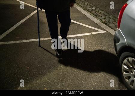 Silhouette und Schatten eines älteren Mannes auf der französischen Straße nachts mit einem Gehstock, der das Gleichgewicht mit blauem Teleskoprohr aus Aluminiumrohr bewahrt medizinische Hilfe und Rehabilitation Stockfoto