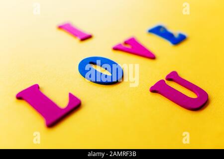 Die Aufschrift "Ich liebe dich auf gelbem Hintergrund", die Buchstaben der modischen hellen Farben klassisch blau und leuchtend pink. Das Konzept des valentinstages, ich liebe dich - Aufschrift aus Holzbriefen. Stockfoto