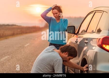 Paar Reparatur Auto Reifens an der Straße im Herbst Sonnenuntergang und Aufruf für Pannenhilfe, selektiver Fokus Stockfoto