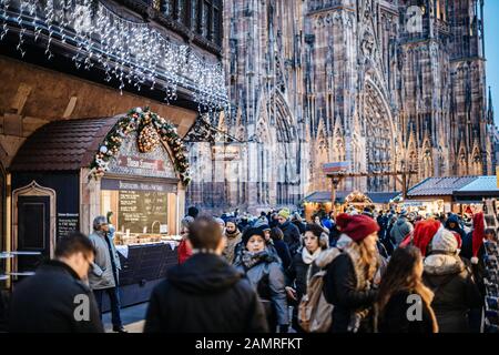 Straßburg, Frankreich - 20. Dezember 2016: Eine große Gruppe von Menschen, die den Weihnachtsmarkt im Zentrum von Straßburg mit der Kathedrale Notre-Dame im Hintergrund und Gourmet-Chalet von Maison Kammerzell entdecken Stockfoto