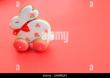 Osterfeiertagskonzept, handgemachte rosa weiße Lebkuchen in Form eines Hasen auf rotem Hintergrund. Lebkuchen Osterhase Kaninchen Stockfoto