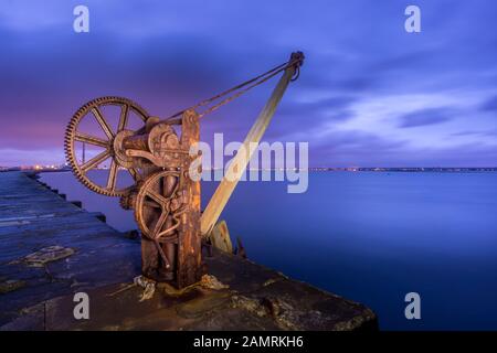 Der alte, rostige manuelle Dockkran am langen Pier, Der Great South Wall, neben dem Poolbeg Lighthouse in Dublin Docks, Irland. Langzeitfotografie Stockfoto