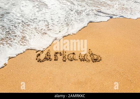 Handgeschriebener Text in deutscher Sprache im Urlaub am goldenen Strand mit kommender Welle. Konzept der Sommerferien und Ferien Stockfoto