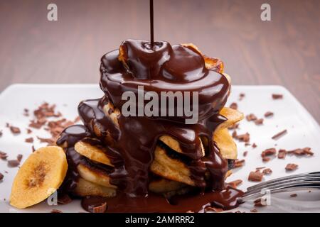 Schokolade gießt auf Pfannkuchen mit Banane auf Holzgrund Stockfoto