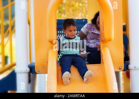 Ein kleiner Junge, der sich an seine großen Schwestern hält, bevor er sich auf eine Rutsche auf dem Spielplatz begeben kann. Stockfoto