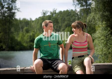 Teenager und Mädchen sitzen neben einem Fluss. Stockfoto