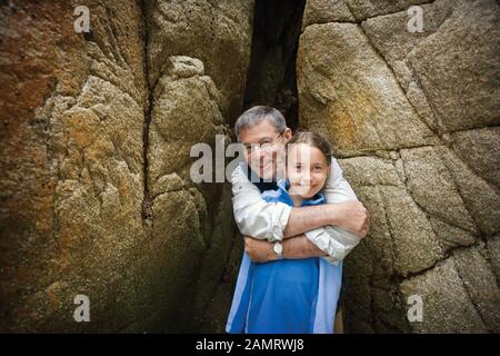 Papa umarmt Tochter vor Felsbrocken Stockfoto