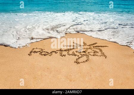 Handgeschriebener Text Portugal und Sonnensymbol auf dem goldenen Strandsand mit kommenden Wellen. Konzept für heiße Sommerferien und Urlaub am Meer oder Meer Stockfoto