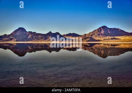 Zerklüftete felsige Berge spiegeln sich im glatten, spiegelähnlichen Wasser der Bonneville Salt Flats im Westen Utahs in den USA wider. Stockfoto