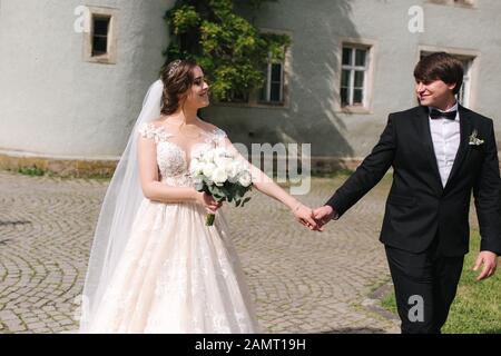 Jungvermählten sind zu Fuß in den Park in der Nähe der großen Burg. Schöne Braut mit stattlichen Bräutigam Stockfoto