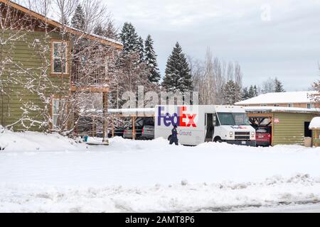 Ein FedEx Fahrer läuft durch starken Schnee zu ihrem LKW, nachdem er im Winter Pakete in eine Wohnung geliefert hat. Stockfoto