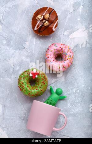 Farbige Donuts auf grauem Hintergrund mit Kaffeebecher. Draufsicht, Donuts verteilen sich über einen Becher, der Rauch aus Kaffee imitiert. Konzept Desserts, süße don Stockfoto