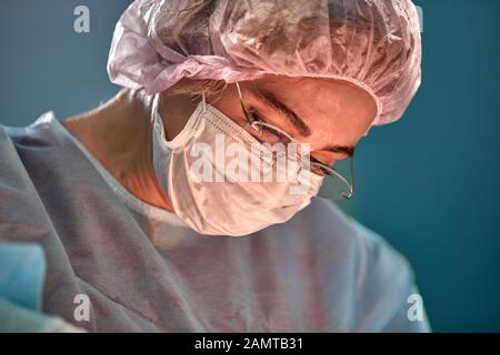 Close up Portrait von jungen weiblichen Chirurg Arzt durch das Tragen von schützender Maske und Hut während der Operation. Gesundheitswesen, medizinische Ausbildung, Chirurgie Konzept. Stockfoto