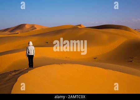 Eine weibliche Touristen bewundert die wunderschönen, goldenen Dünen in der Wüste von Merzouga, Marokko Stockfoto