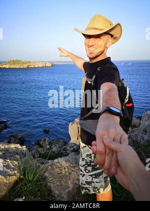 Mann, der auf Küstenfelsen steht und die Hand seiner Freundin, Mellieha, Malta, hält Stockfoto