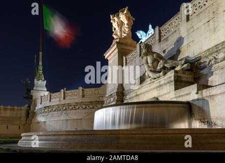 ROM, Italien - 25. März 2018: Die italienische Flagge fliegt nachts über einem Brunnen auf dem Vaterländischen Altar in Rom. Stockfoto