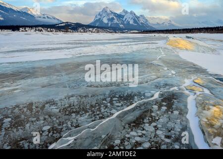 Eingeschlossene Methanblasen, die unter dem dicken gerissenen und gefalteten Eis am Abraham Lake ins Wasser gefroren waren Stockfoto