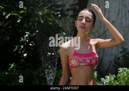 Teenager-Mädchen, das in einem Garten steht und sich mit einem Wasserschlauch abkühlt, Argentinien Stockfoto