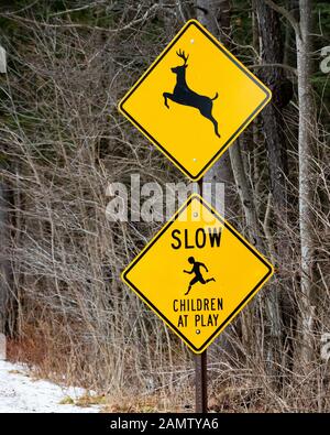 Ein 'Deer Kreuzung' Zeichen über eine niedrige Kinder beim Spielen' Zeichen auf der Seite einer Straße in der Spekulant, NY, USA Stockfoto