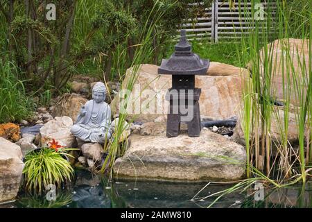 Graue buddha-skulptur und Pagode am Rande des Teiches mit Typha - Cattail Pflanzen im Zen-Garten im Sommer an der Route des Gerbes d'Angelica Garten. Stockfoto