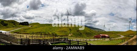 Landwirtschaftliches Panorama eines Bauernhofes und seiner Schaf- und Viehhöfe auf den Hügeln und Tälern mit Strom erzeugenden Windkraftanlagen auf den Gipfeln Stockfoto