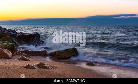 Wellen, die bei Sonnenuntergang auf der felsigen Küste abstürzen Stockfoto