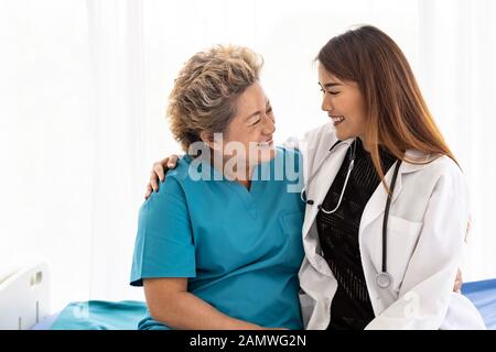Junge weibliche Arzt in Uniform umarmen und lächelnd auf alte ältere Frau Patienten bei einem Besuch im Krankenhaus Stockfoto