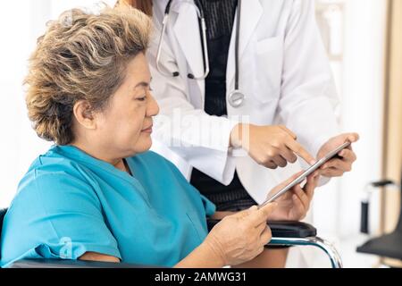 Asiatische vertrauen Arzt mit digitalen tablet Ausdruck Gesundheit Interessen mit alten ältere Frau Patienten sitzen auf Rollstuhl Stockfoto