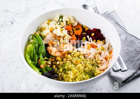 Gesunde Mittagsschüssel. Salat mit Fleisch, Käse, Bulgur und Gemüse auf Marmorgrund. Nahaufnahme Stockfoto