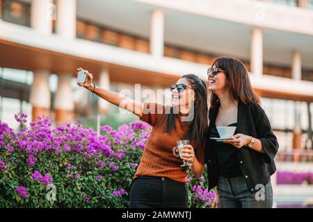 Zwei hübsche Frauen stehen und machen selfie mit ihren Getränken. Stockfoto