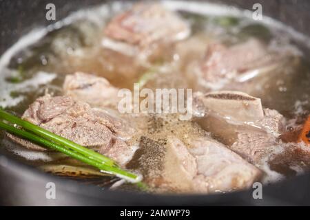 Traditionelle Rinderbrühe mit Gemüse, Knochen und Zutaten im Topf, Kochrezept. Suppe in einem Kochtopf mit Pfanne auf dunklem Steingrund. Oben Stockfoto