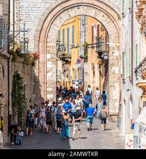 Assisi, Italien - 29. August 2018: Straße in Umbrien und Menschen, die während des sonnigen Sommertags im historischen Dorf St Francis unter Bogen spazieren Stockfoto