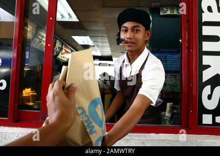 Antipolo City, Philippinen - Januar 11, 2020: Arbeitnehmer in einem Fast Food Restaurant das Essen Bestellung eines Kunden bei einem Drive Thru Fenster. Stockfoto