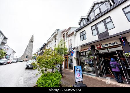 Reykjavik, Island - 19. Juni 2018: Fußgänger, die auf der Straße mit nasser Straße und Gehweg in der Innenstadt und berühmter Kirche und Icemart laufen Stockfoto