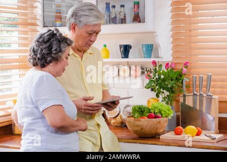 Asiatische senior Paar mit Tablet-PC zu suchen Menü Rezept und Art von Gemüse in der Küche zu Hause. Senior mit Technologie lfiestyle. Altern mit Stockfoto