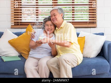 Asiatische älterer Mann überraschen ältere Frau mit Geburtstag Kuchen im Wohnzimmer zu Hause. Altern zu Hause Konzept. Stockfoto