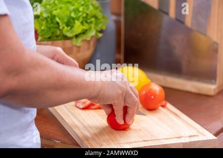 Geschlossen bis senior Hand schneiden Tomaten auf Holz Schneidebrett. Vorbereitung von Salat, gesunden Ruhestand lifestyle Konzept. Stockfoto