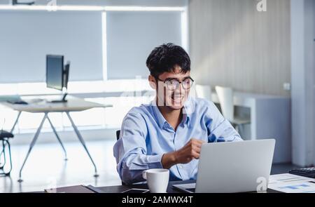 Asiatische Geschäftsmann, Arme, Erfolge zu feiern, wenn Auftrag Infornt von Laptop auf dem Schreibtisch in modernen Büro getan ist. Stockfoto