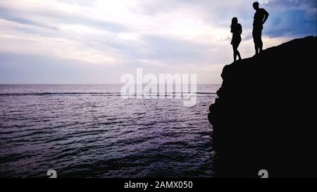 Liebendes Paar steht am Rande des Felsens und bereitet sich auf den Sprung ins Wasser vor, romantisch Stockfoto