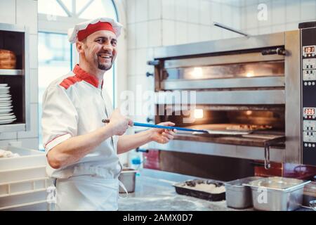 Lächelnder Koch, der in einer Restaurantküche Pizza in den Ofen legt Stockfoto