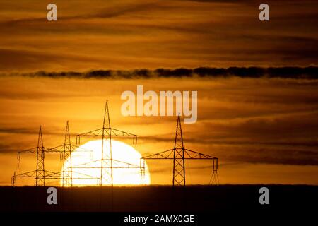 15. Januar 2020, Baden-Württemberg, Schwieberdingen: Die Sonne steigt hinter Hochspannungspylonen auf. Foto: Sebastian Gollnow / dpa Stockfoto